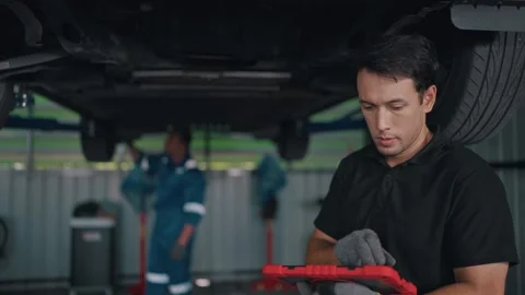 Mechanic inspects EV car underside with tablet Stock-Footage 341461501