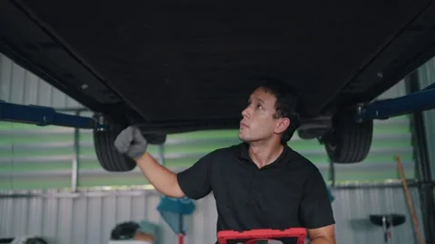 Mechanic inspects EV car underside under lift Stock-Footage 341461727