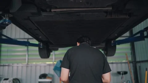 Mechanic inspects EV car underside under lift Stock-Footage 341461879