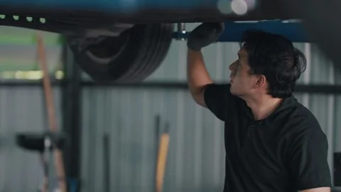 Mechanic inspects EV car underside under lift Stock-Footage 341461955