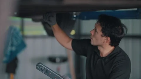 Mechanic inspects EV car underside under lift Stock-Footage 341461958