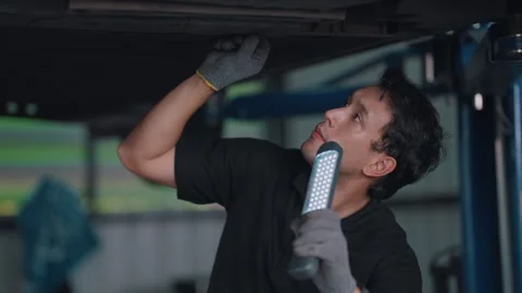 Mechanic inspects EV car underside under lift Stock-Footage 341461971