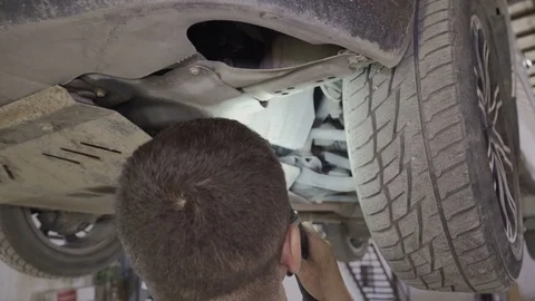 A mechanic inspects with a flashlight the bottom of a car on a car lift Stock Footage 126111177