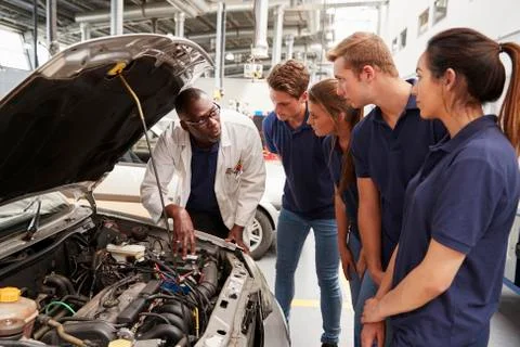 Mechanic instructing trainees around the engine of a car Stock Photos