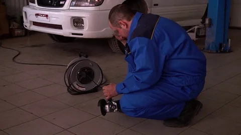 Mechanic in lab coat saws angle grinder in the garage on the background of the Stock Footage 75688154