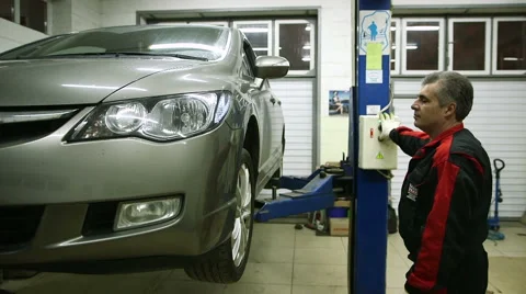 Mechanic lowers the machine holding the button lift Stock Footage 62520914