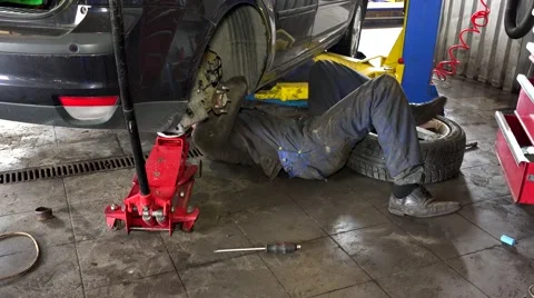 Mechanic lying and working under car at repair garage Stock Footage 65145344