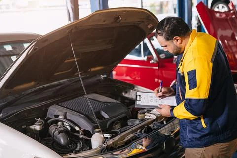 Mechanic man checking engine open hood looking check list car maintenance s.. Fotos de archivo
