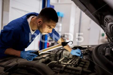 Mechanic man with lamp repairing car at workshop Stock Photos
