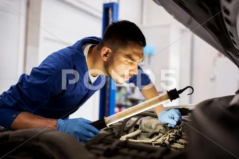 Mechanic man with lamp repairing car at workshop Stock Photos