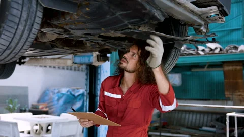 Mechanic man standing, inspecting a raised car, checking condition problem .. Stock Footage 241914864