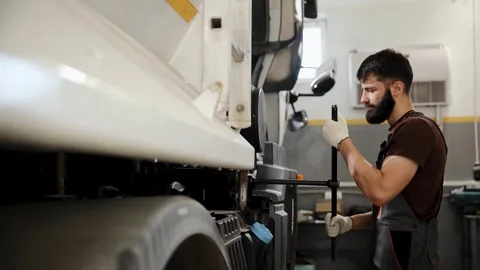 Mechanic man in uniform and work gloves changing a truck wheel in a garage Stock Footage 333705821