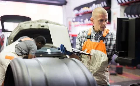 Mechanic man using laptop checking car in workshop Stock Photos
