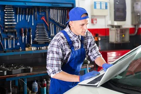 Mechanic man using laptop checking car in workshop Stock Photos