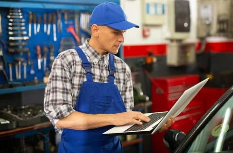 Mechanic man using laptop checking car in workshop Foto stock
