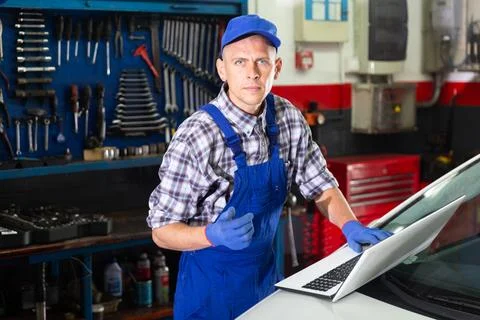 Mechanic man using laptop checking car in workshop Stock Photos