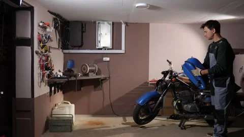 Mechanic man wearing work gloves installing a fuel tank onto a blue motorcycle Stock Footage 342771309