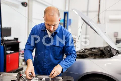 Mechanic man with wrench repairing car at workshop Stock Photos