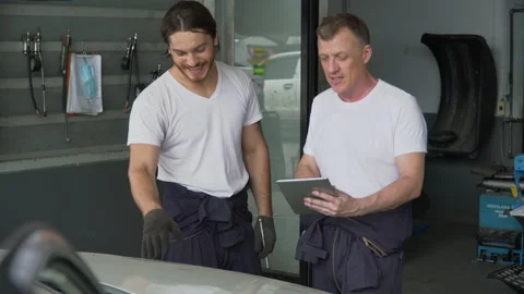 Mechanic manager man checking car with assistant worker using tablet in works Stock Footage 147369080