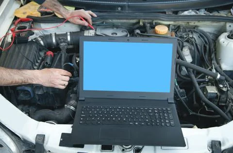 Mechanic with a multimeter testing car engine. Laptop on car engine. Car serv Stock Photos