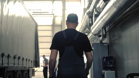 A mechanic in overalls walks through the workshop along a cargo trailer Stock Footage 152254535