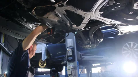 Mechanic performs repair task on underside of car using lighting Stock Footage 317628711