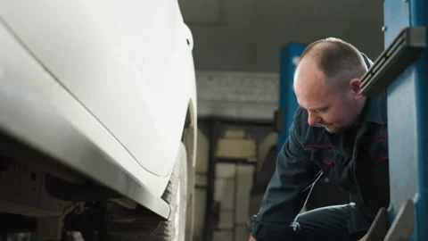 Mechanic Positions Jack Under White Vehicle in Workshop Stock Footage 304972976