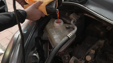 Mechanic pouring red antifreeze coolant liquid into car engine Stock Footage 345106944