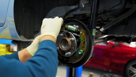 Mechanic in protective gloves repairs wheel hub and disk brakes on car, car is Stock Footage 321445831
