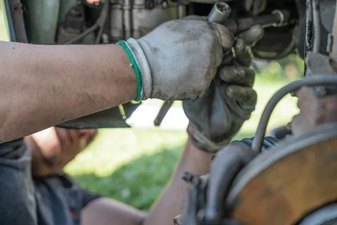 Mechanic in protective gloves using hand tools to work on car undercarriage.. Stock Photos