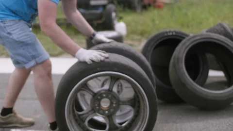 A mechanic puts two wheels on silver rims on the road, one on top of the other Stock Footage 129913926