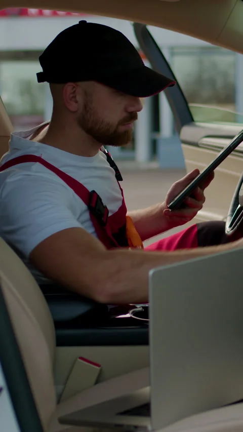 Mechanic in red overalls using laptop inside vehicle, discussing vehicle issues Stock Footage 318346322