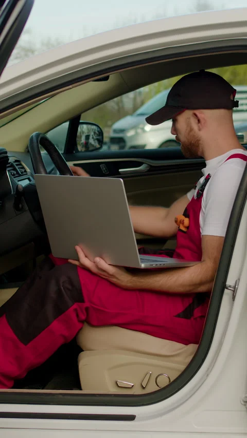 Mechanic in red overalls using laptop inside car, discussing vehicle issues with Stock Footage 320394047