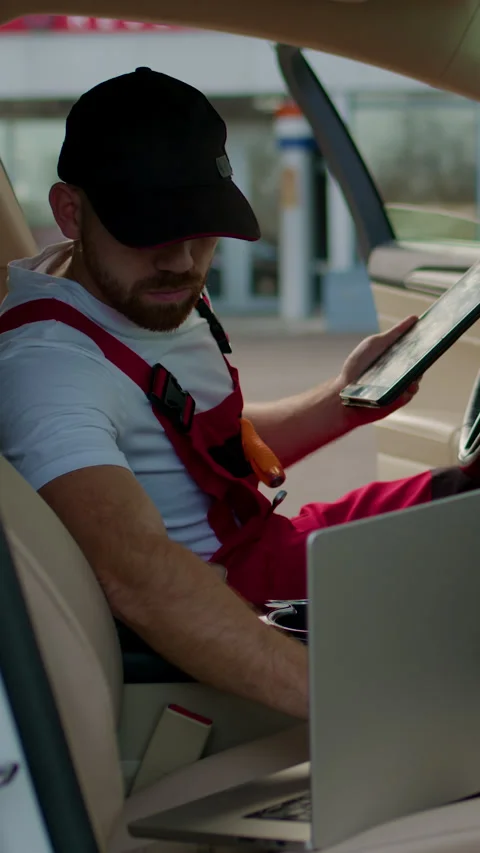 Mechanic in red overalls using a tablet inside a modern car, analyzing vehicle Video stock 320394144