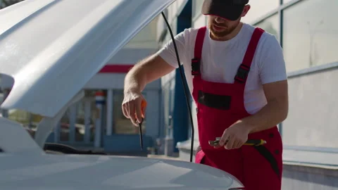 Mechanic in red overalls working on car engine with diagnostic tool, showcasing 스톡 동영상 312516414