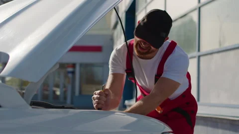 Mechanic in red overalls working on car engine with tools, focused on vehicle 스톡 동영상 312516526