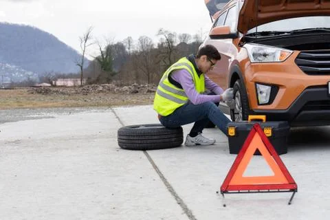 A mechanic in a reflective vest changes a wheel on the road Stock Photos