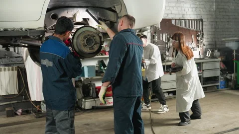 Mechanic Repairing Car While Lab Technicians Observe and Take Notes in Workshop Stock Footage 304973166