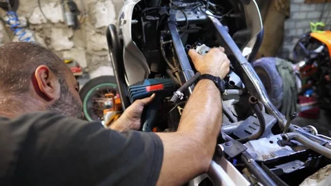 Mechanic repairing engine of motorcycle at workshop. Repairman working at garage Stock Footage 296628640