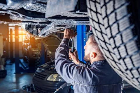 Mechanic repairs car chassis using a car lift. Auto service station backgroun Stock Photos