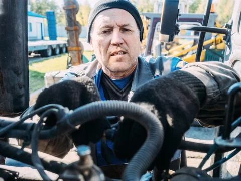 Mechanic repairs engine of tractor or heavy equipment. Farmer inspects and Stock Photos