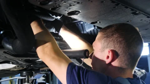 Mechanic repairs underbody of car using flashlight to see area Stock Footage 317628588