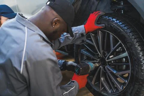 A mechanic replacing car wheels using an electric wrench tyre mounting equipment Stock Photos