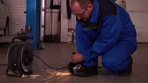Mechanic in robe saws angle grinder in the garage on the background of the car Stock Footage 75688197