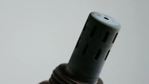 Mechanic rotating a worn oxygen sensor against a white background. Grime and Stock Footage 283694800