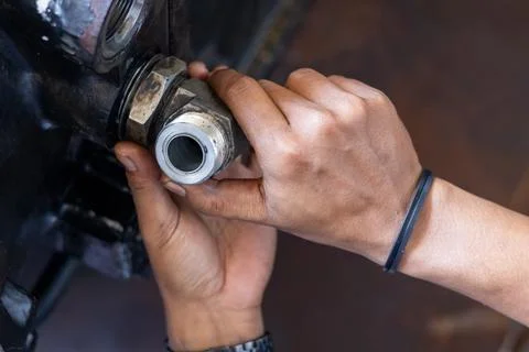 Mechanic screws threaded elbow pipe fitting into heavy transmission housing.. Stock Photos
