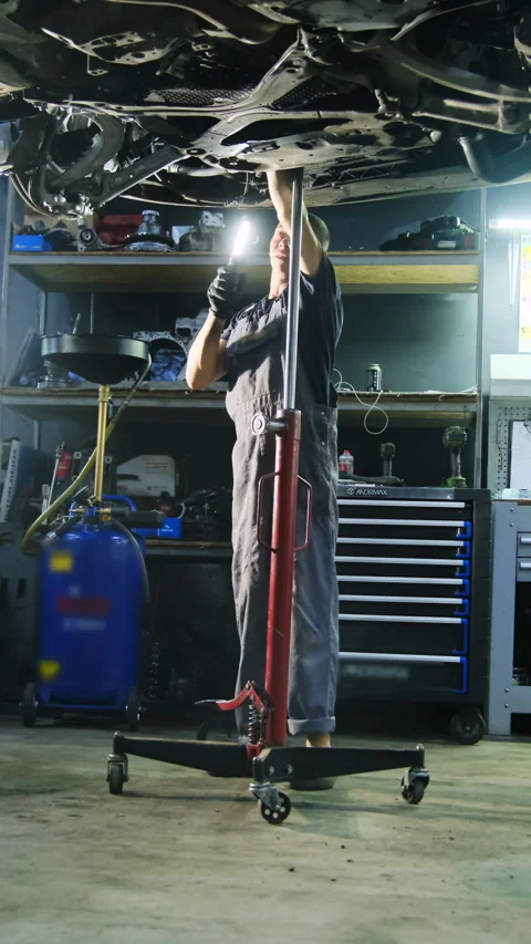 Mechanic shines flashlight and inspects underside of automobile Stock Footage 317653553