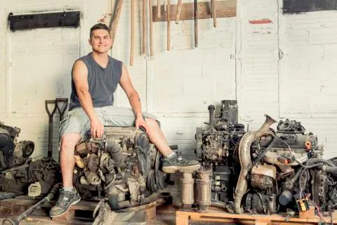 Mechanic sitting on a car engine with multiple engines around it. Stock Photos