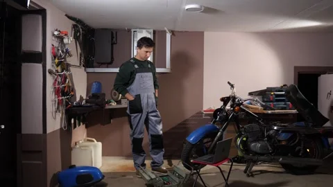 Mechanic standing in a garage, looking down at an open toolbox and a laptop Stock Footage 342765083