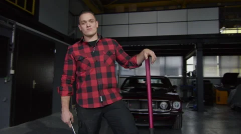 Mechanic standing outside his workshop, while camera pans towards him Stock Footage 63026591